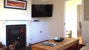 A living room with a fireplace, a television mounted on the wall, a table with a book, and a sofa. - Hedgelea (Okehampton)