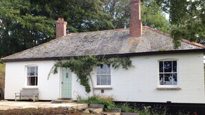 A white cottage with a green door, a bench outside, and a stone wall in front. - Hedgelea (Okehampton)