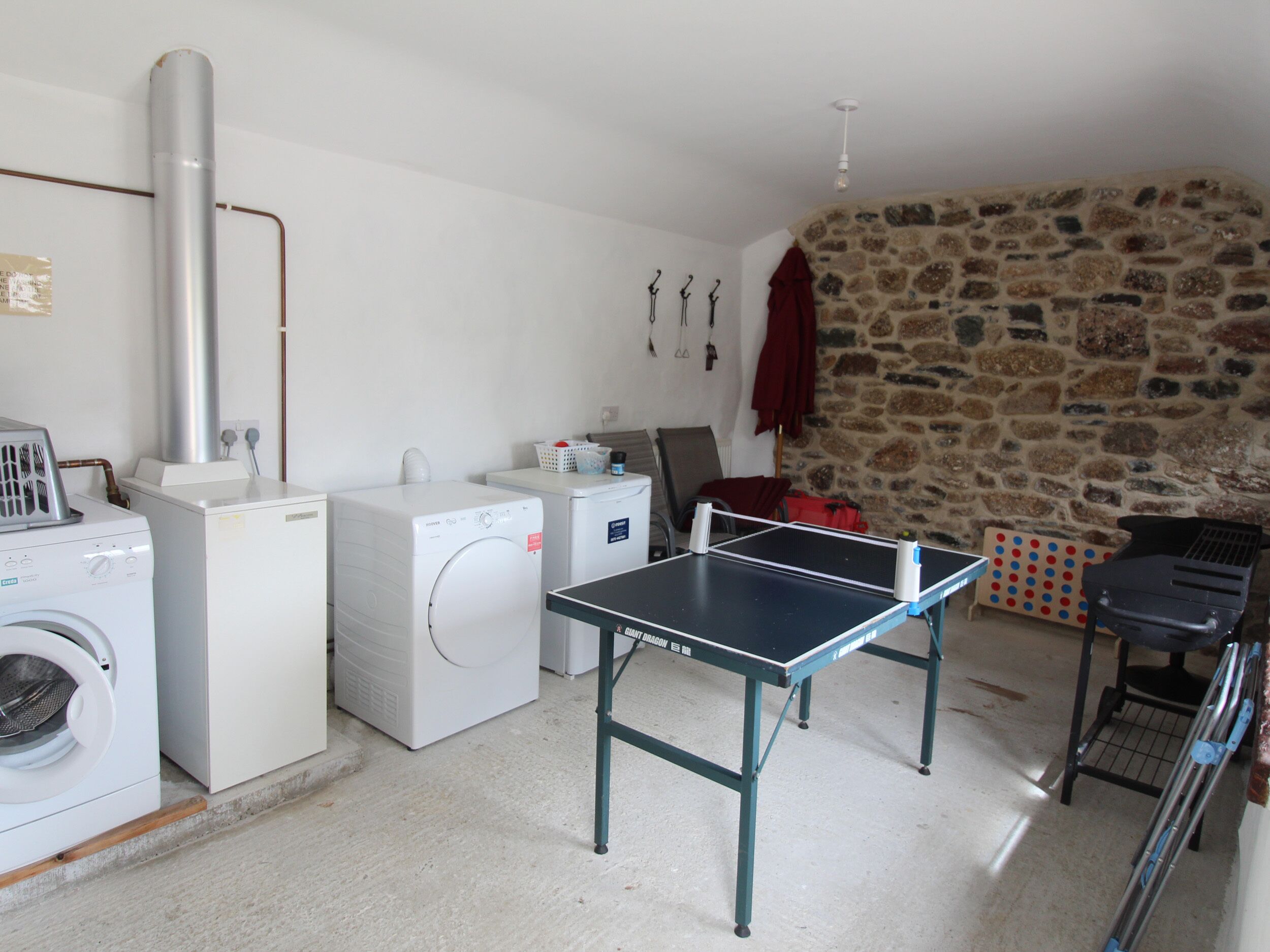 A laundry area with washing machines, a drying machine, a table tennis table, and a stone wall.