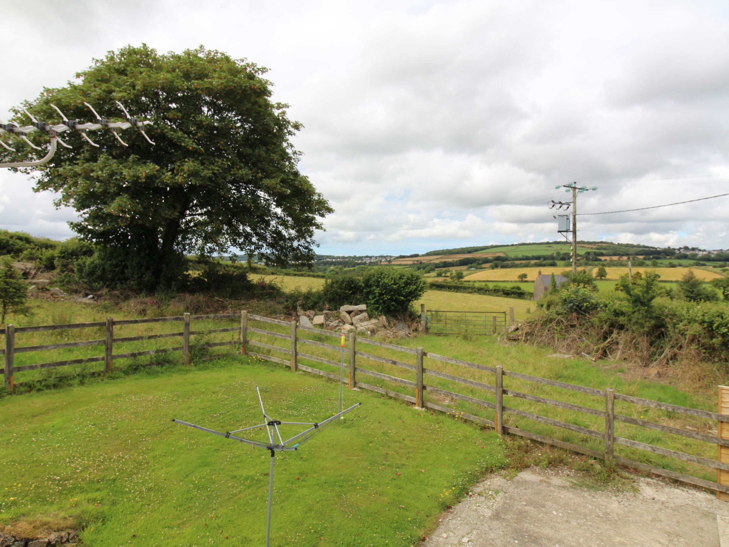 A rural landscape with a large tree, a wooden fence, and a metal structure in the foreground.