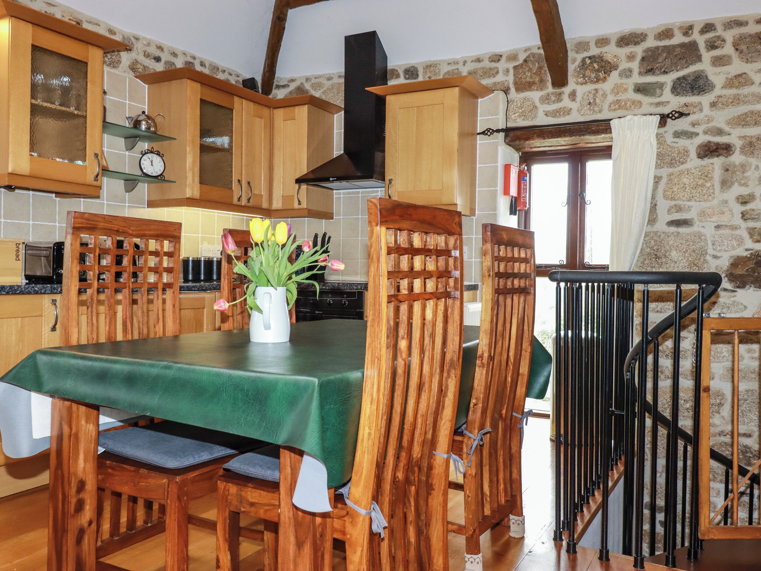 A rustic kitchen with wooden cabinets, a stone wall, and a dining table with chairs.