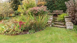A garden with a stone wall, a wooden bench, and various plants. - Coverdale Cottage (Leyburn)