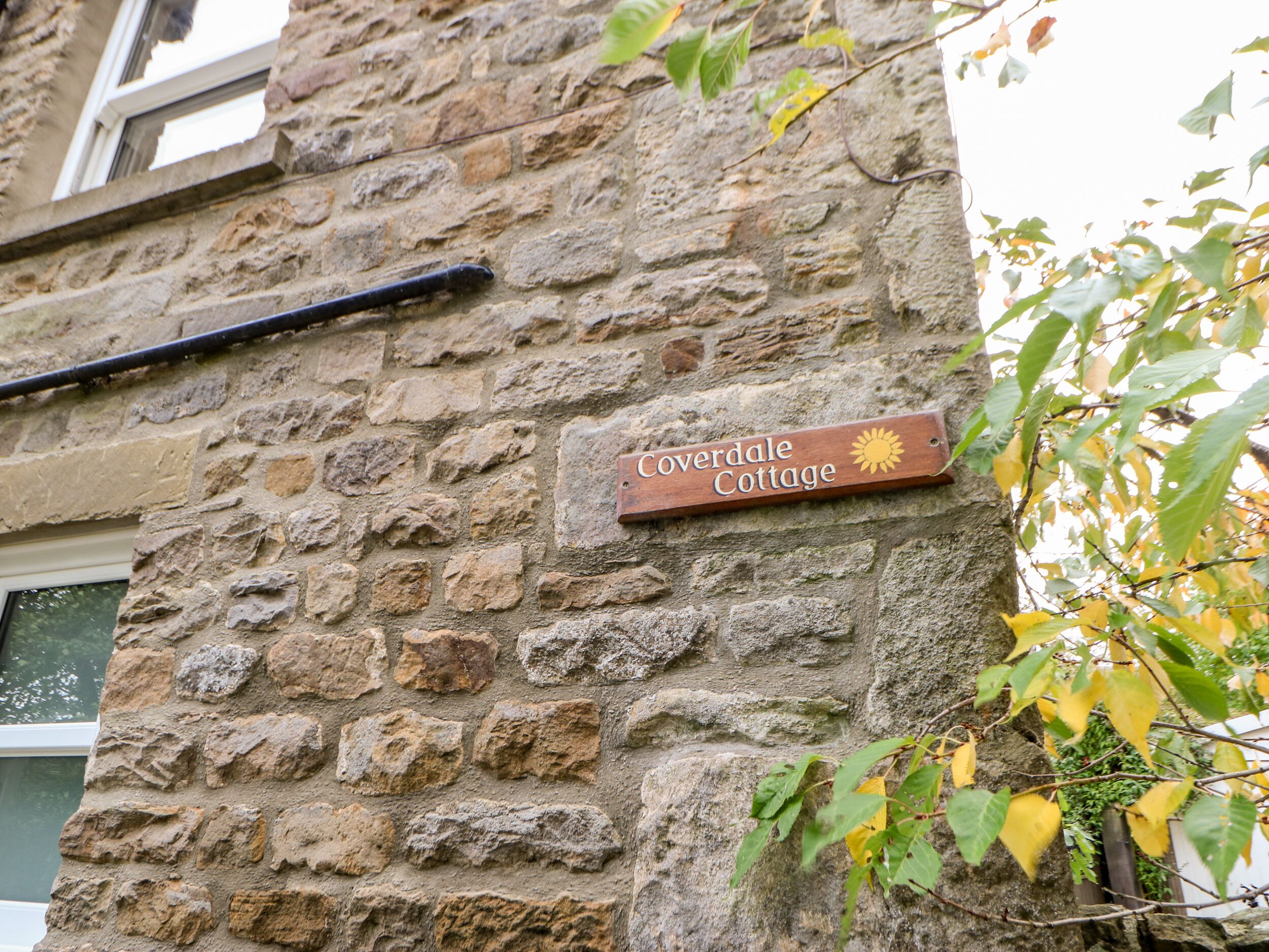 Un mur de pierres sur lequel est fixée une plaque en bois portant l’inscription « Coverdale Cottage ».