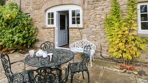 A stone building with a round table and chairs, a door, and potted plants. - Coverdale Cottage (Leyburn)