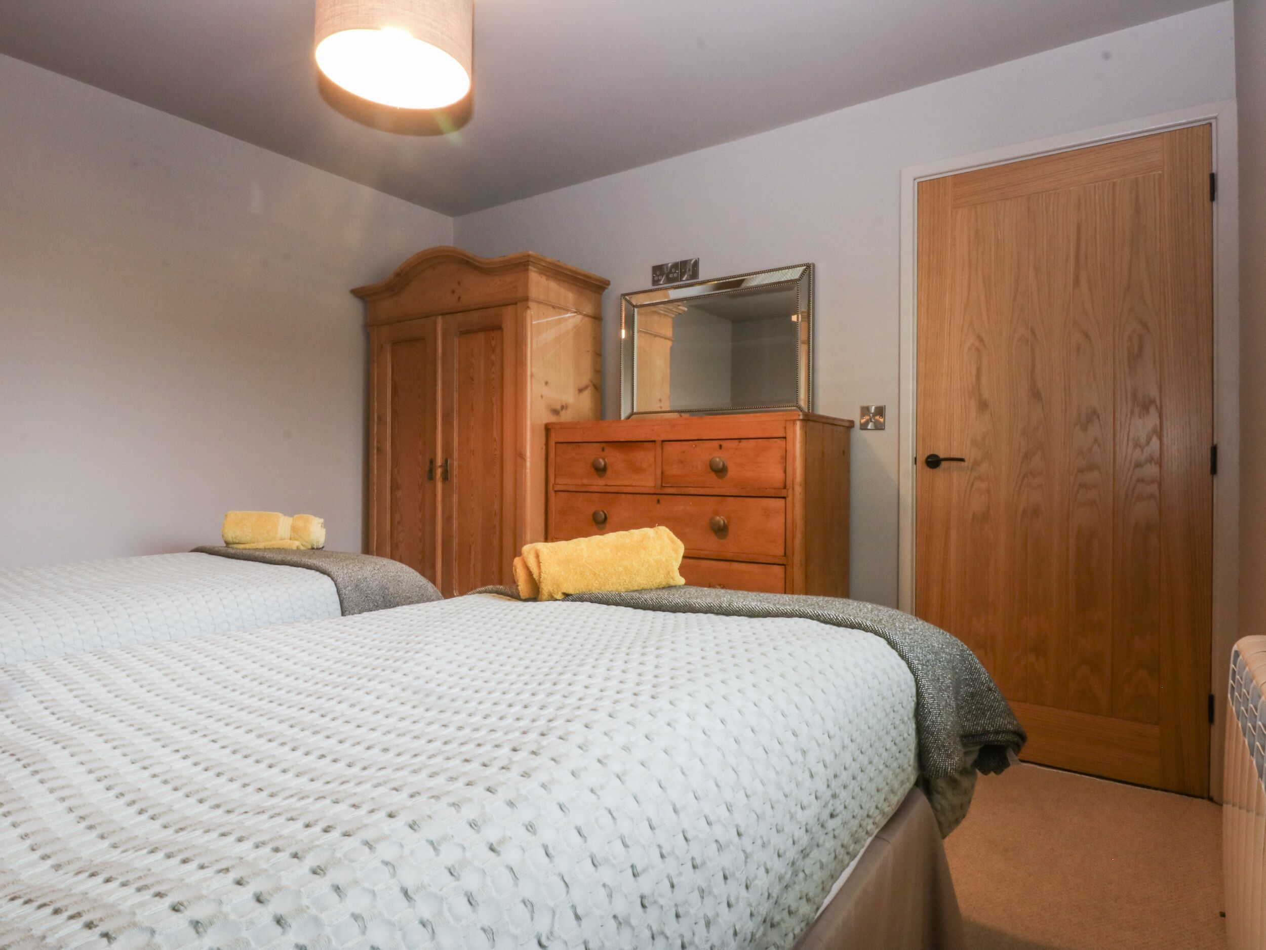 Een slaapkamer met twee bedden, een houten garderobe en een spiegel.