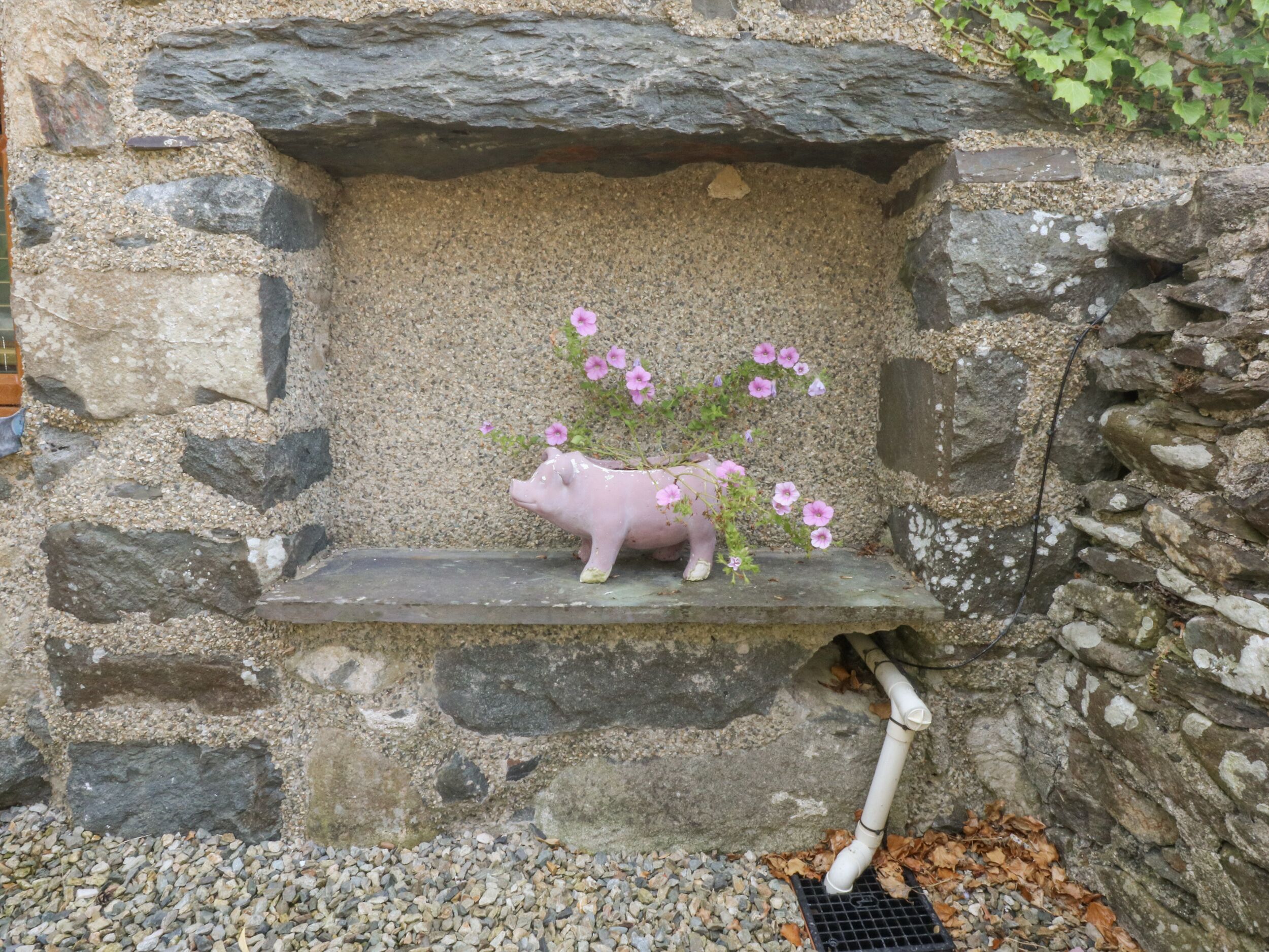 Eine Steinmauer mit einem Sparschwein-Blumentopf, der rosa Blumen enthält.
