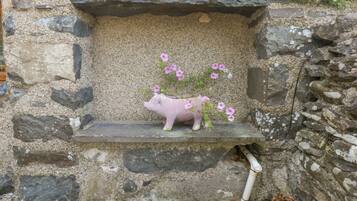 Eine Steinmauer mit einem Sparschwein-Blumentopf, der rosa Blumen enthält.