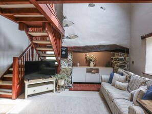 A cozy living room with a wooden staircase, a flat-screen TV, a sofa, and a stone wall. - Cegin Foch (Pwllheli)