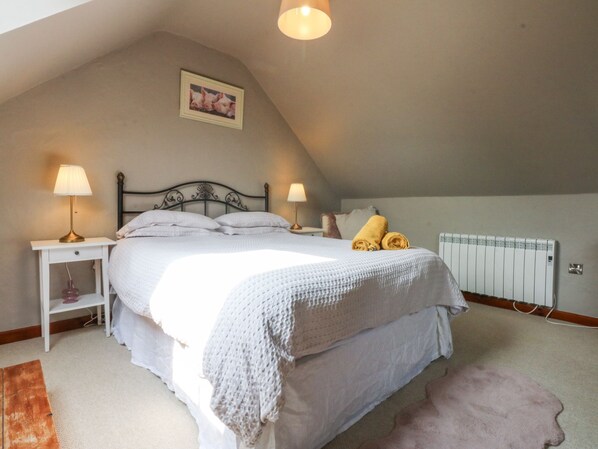 A bedroom with a bed, two bedside tables with lamps, a radiator, and a picture on the wall. - Cegin Foch (Pwllheli)