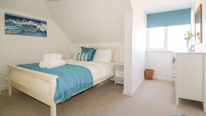 A bedroom with a bed, bedside tables, a dresser, a window, and a painting on the wall. - Offshore (Newquay)