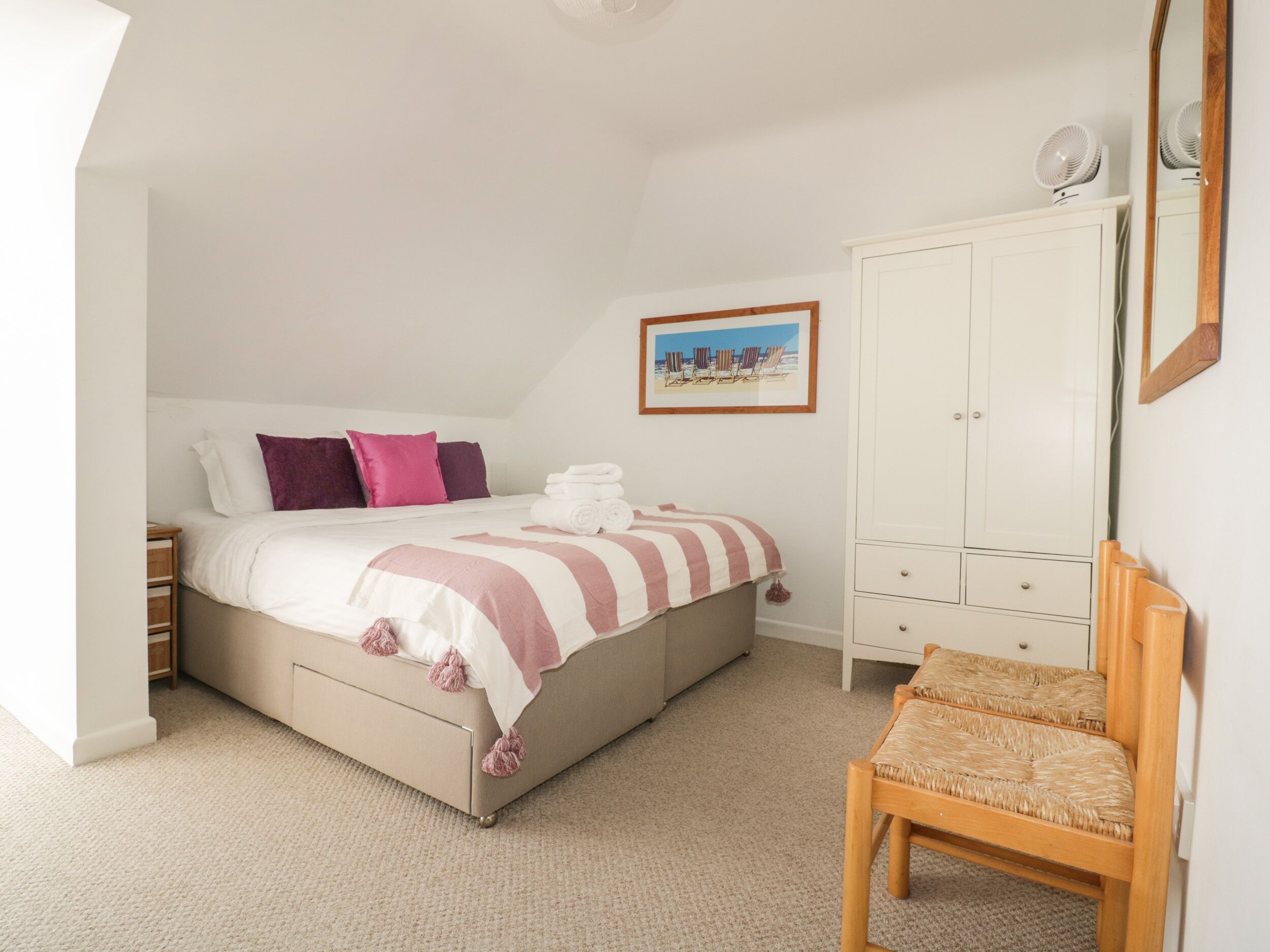 A bedroom with a bed, a wooden chair, a wardrobe, and a framed picture on the wall.