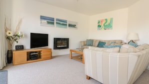 A living room with a sofa, a coffee table, a TV, a fireplace, and wall art. - Offshore (Newquay)