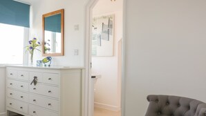 A white dresser with multiple drawers, a mirror, and a vase with flowers. - Offshore (Newquay)