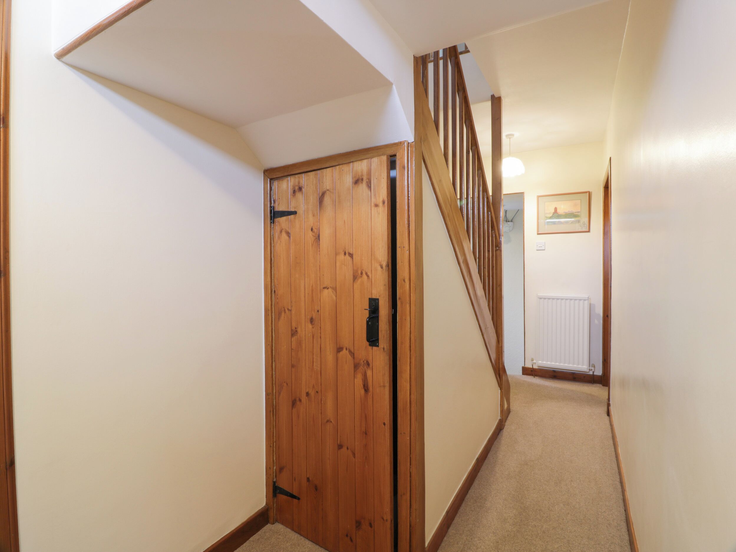 A wooden door with a black handle, a carpeted floor, and a staircase with wooden railings leading to another room.