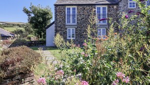 Une maison en pierre dotée de nombreuses fenêtres et d’un jardin où poussent différentes plantes et fleurs.