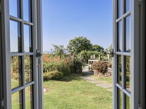 A view through open glass doors into a garden with a stone wall, a wooden pergola, and a variety of plants and flowers. - Atlantic View (Tintagel)