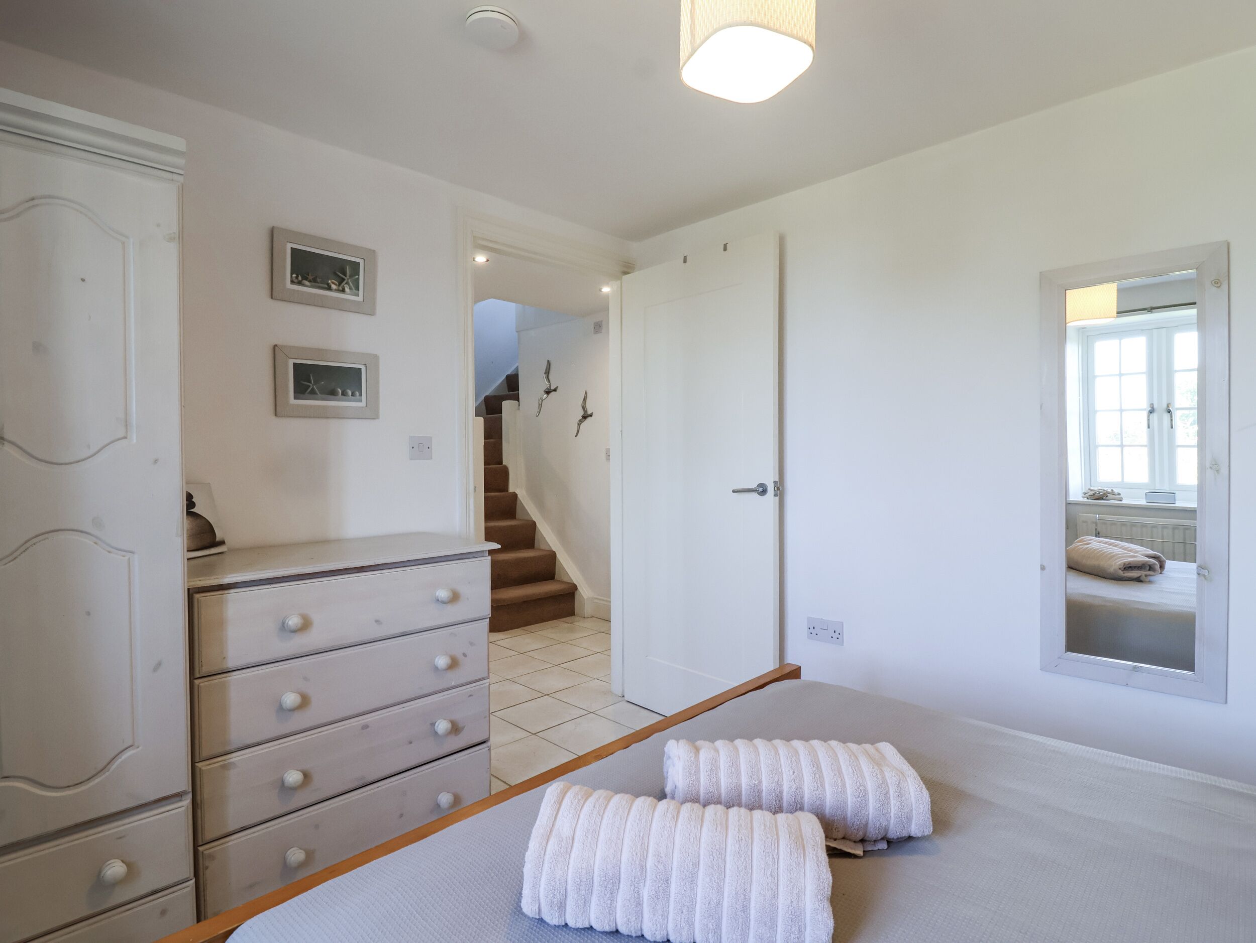 Quarto com cama, penteadeira, janela e escada para outro cômodo.