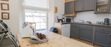 A modern kitchen with grey cabinets, a wooden countertop, and a window with blinds.