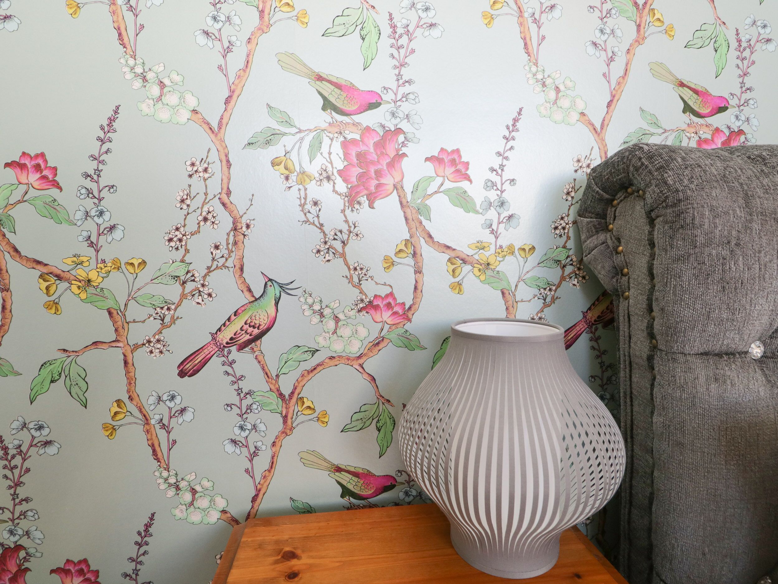 Une pièce avec un papier peint à motifs floraux, une table d’appoint en bois et un vase.