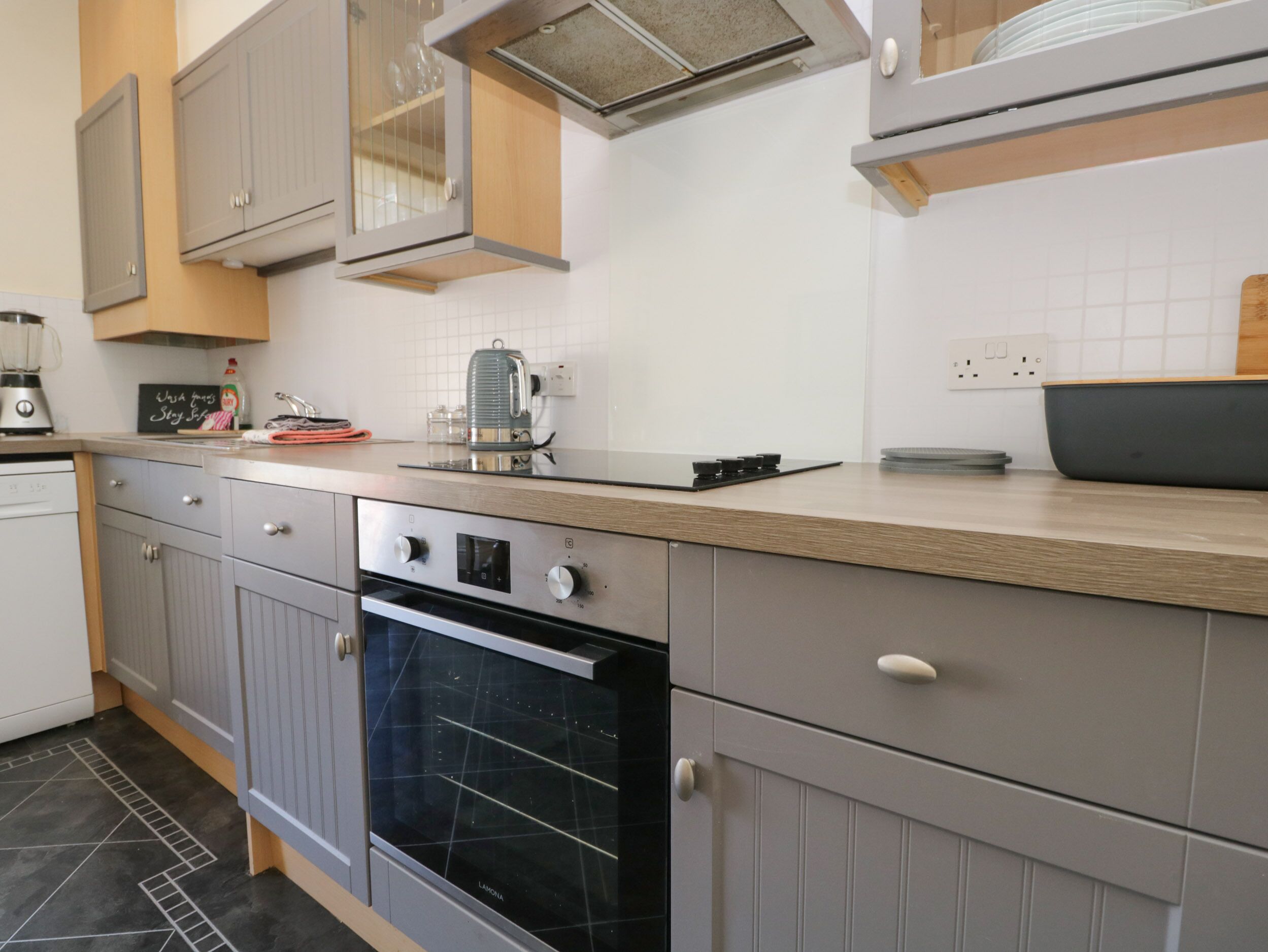 A kitchen with grey cabinets, a black oven, a coffee maker, and a kettle on the countertop.