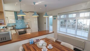 Una cocina moderna con encimeras de madera, una mesa de comedor preparada para cuatro personas y un ventanal con persianas.