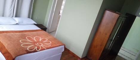 A hotel room with a bed, a wooden wardrobe, and a window with curtains.