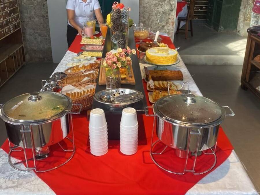 Una mesa de buffet con diversos alimentos y bebidas, una persona sirviendo y un mantel rojo.
