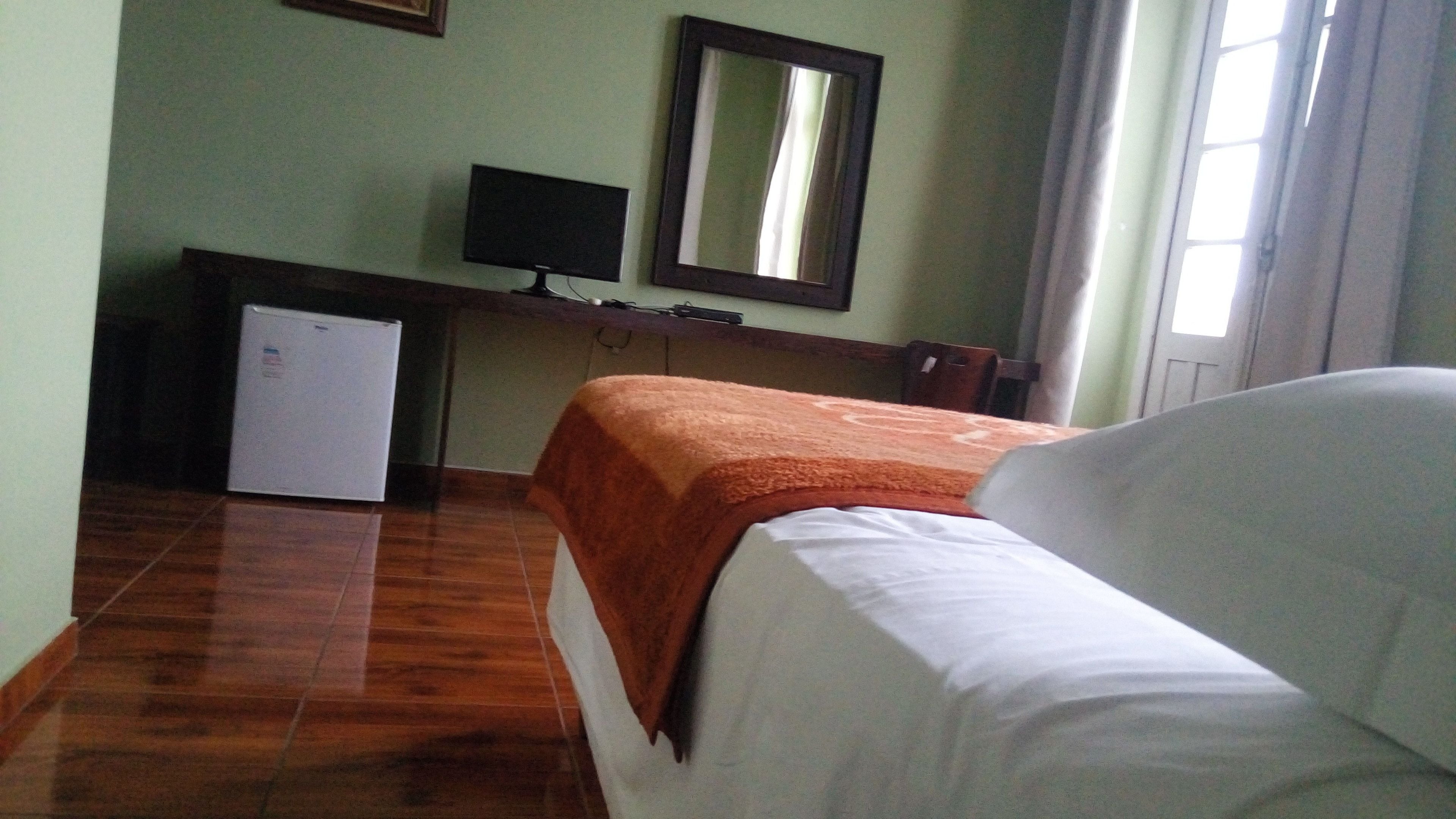 A hotel room with a bed, a small desk with a television, and a refrigerator.