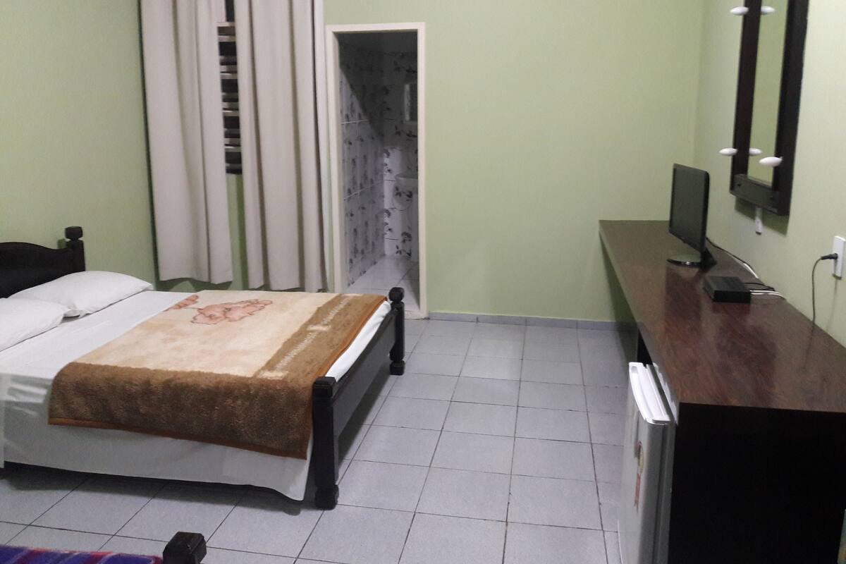A bedroom with a bed, a desk, a computer, and a mirror.