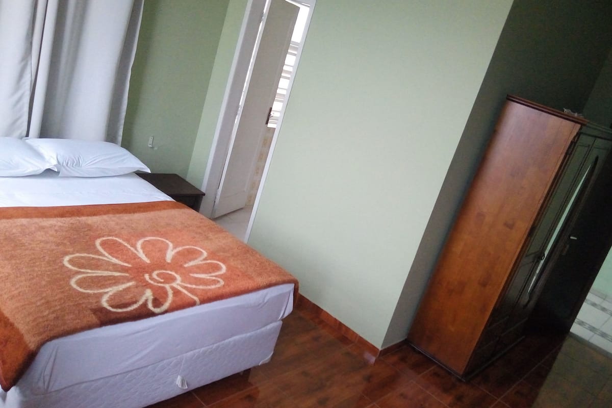 A bedroom with a bed, a wooden wardrobe, and a window with curtains.