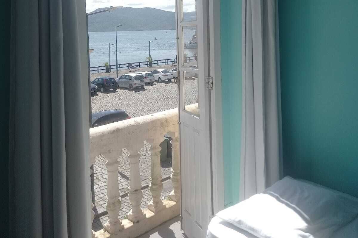 A room with a balcony overlooking a beach, a bed, and a view of the sea and mountains.