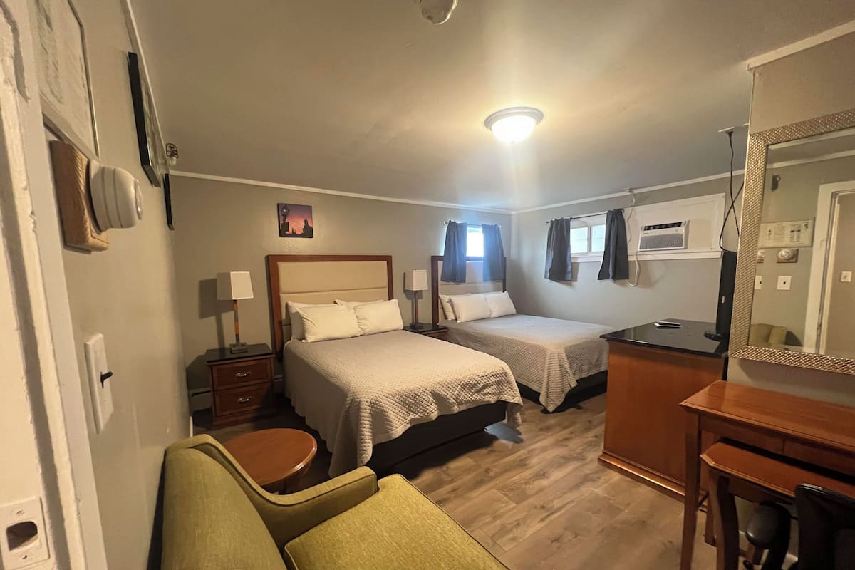 A hotel room with two beds, a desk, a chair, and a mirror.