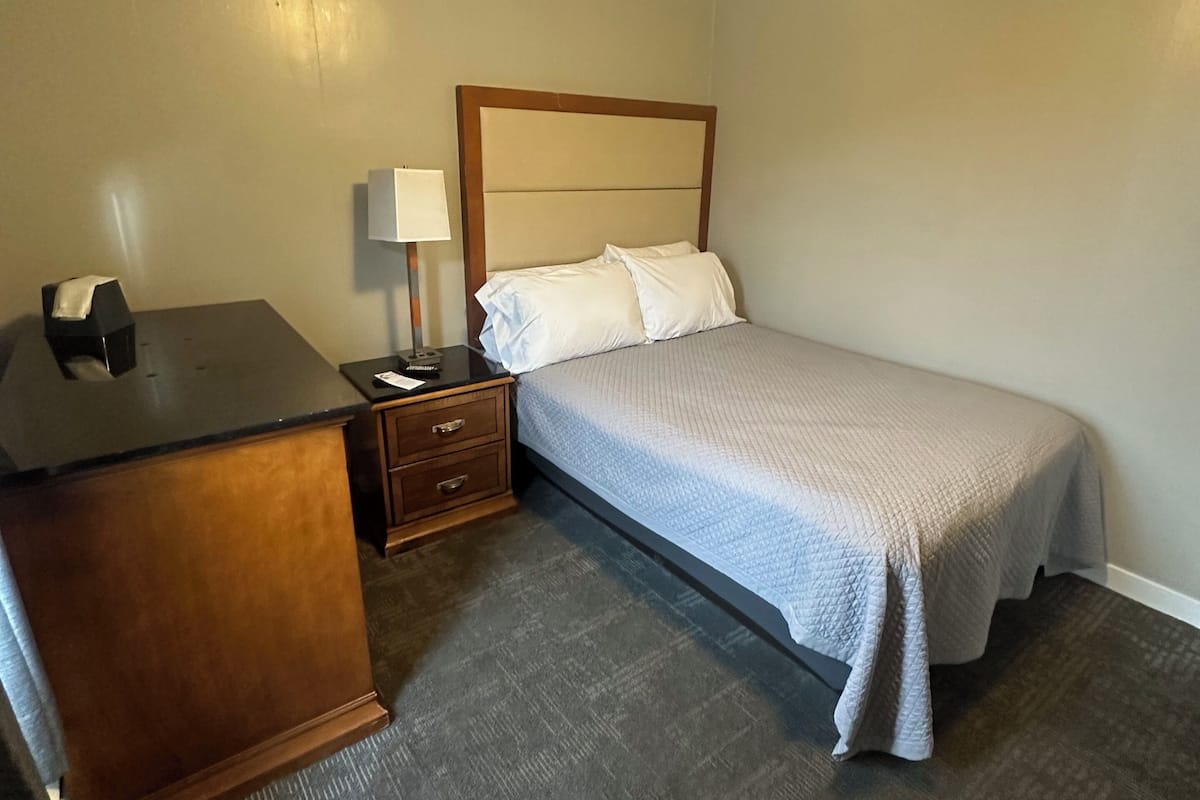 A bedroom with a bed, a nightstand, a desk, and a lamp.