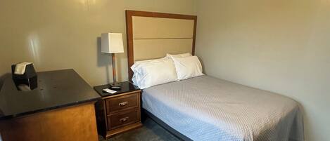 A bedroom with a bed, a nightstand, a desk, and a lamp.