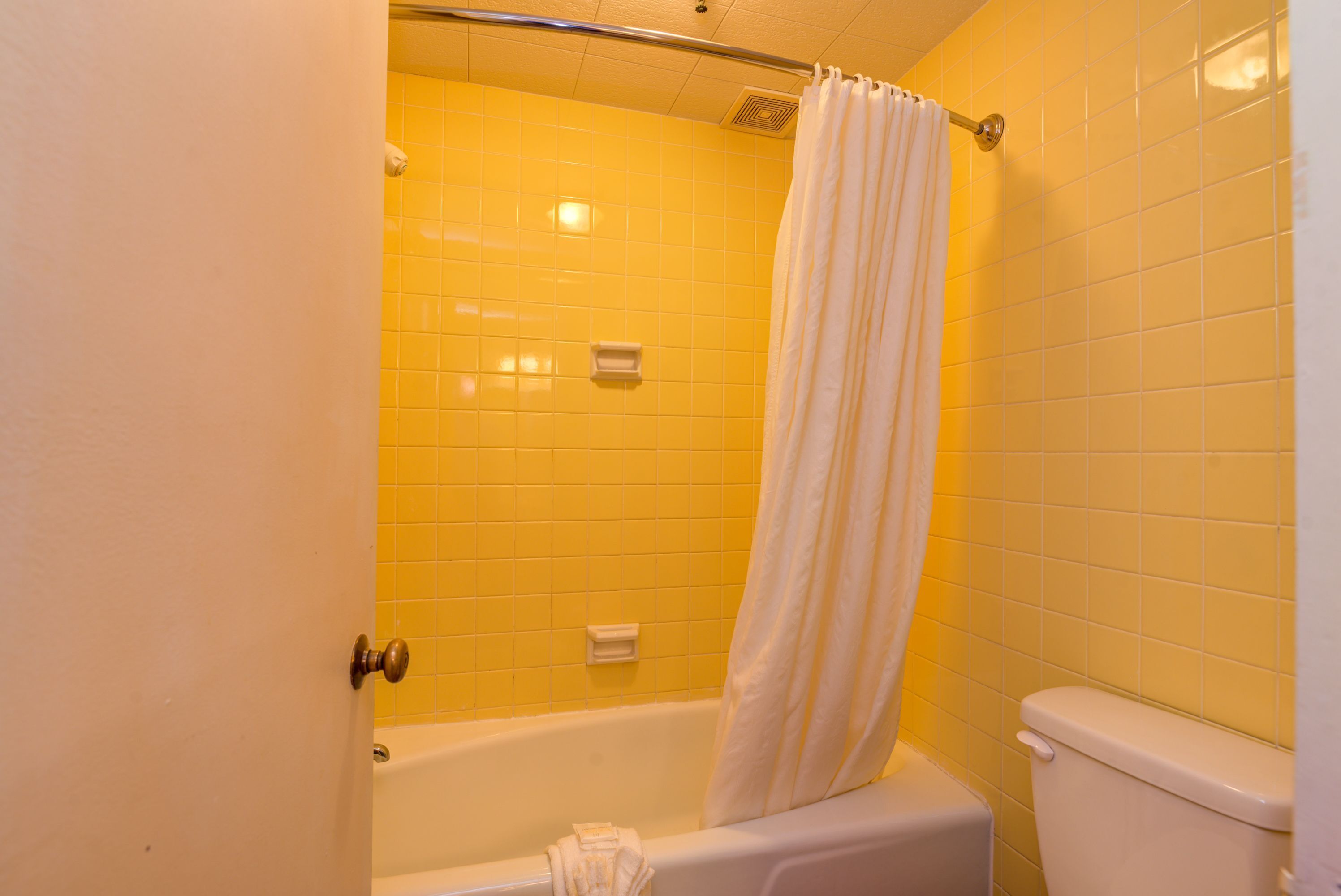 A bathroom with yellow tiles, a white bathtub, and a white toilet.