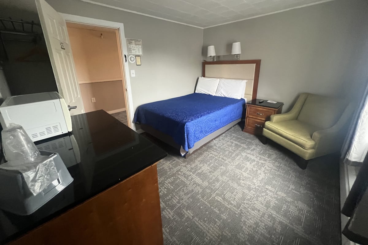 A hotel room with a bed, a desk, a chair, a nightstand, and a wardrobe.