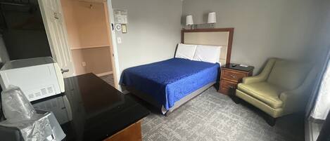 Habitación de hotel con cama, escritorio, silla, mesita de noche y armario.