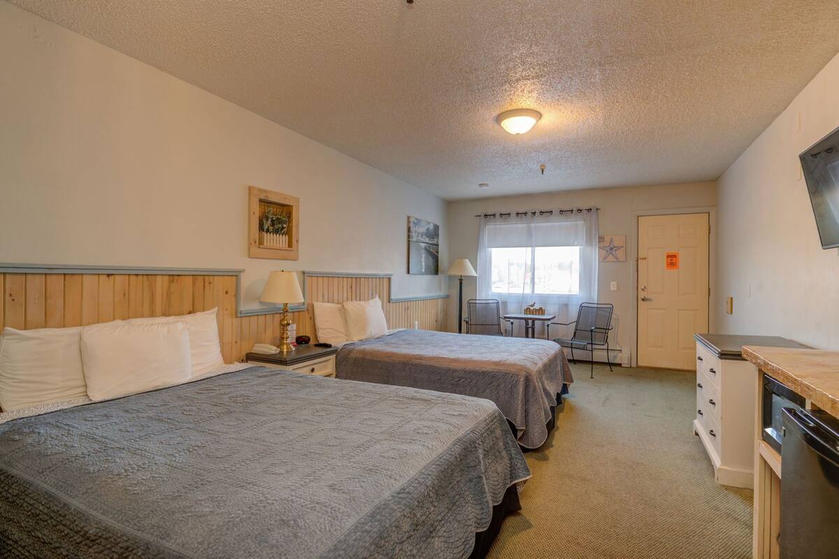 A hotel room with two beds, a desk, a chair, a television, and a window with curtains.