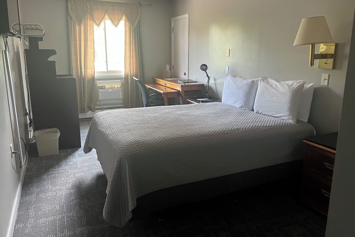 A hotel room with a bed, desk, chair, and a window with curtains.