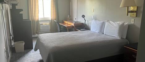 Ett hotellrum med en säng, ett skrivbord, en stol och ett fönster med gardiner.