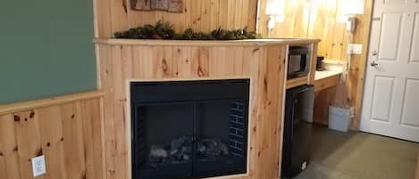 Interior de una cabaña con pared de madera, chimenea, microondas y una puerta.