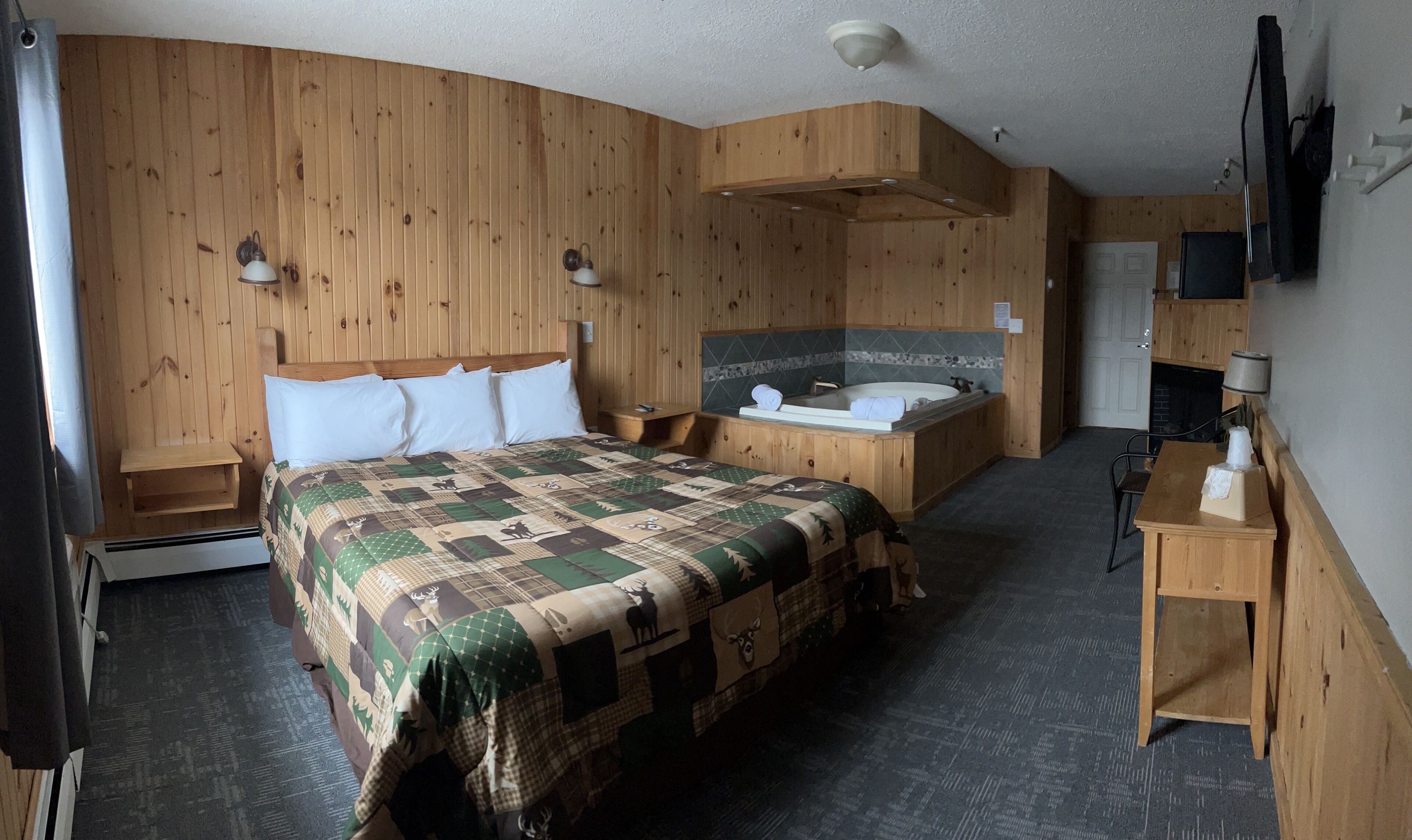 A wooden room with a bed, a wooden bench, a small table, a bathtub, and a TV mounted on the wall.