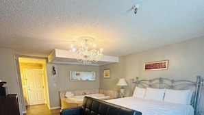 Une chambre à coucher avec un lit, un canapé en cuir noir, un lustre, une table de chevet et un miroir.