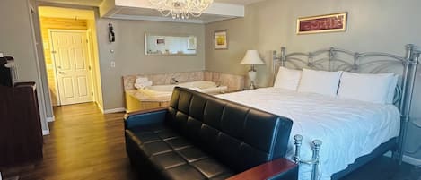 A bedroom with a bed, a black leather sofa, a chandelier, a bedside table, and a mirror.