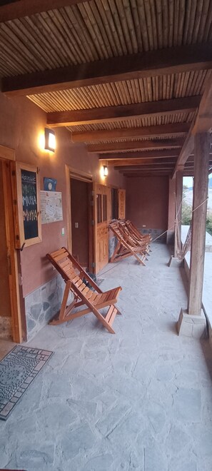 A covered outdoor area with wooden loungers, a stone floor, and a wooden ceiling.