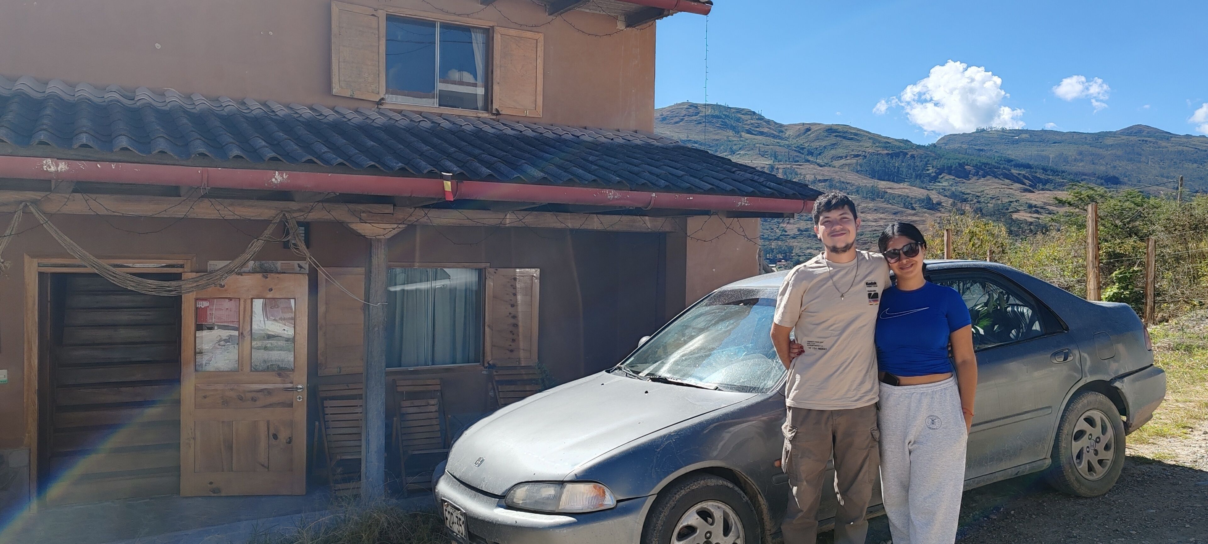 A building with a corrugated metal roof, a wooden door, and a car parked in front.