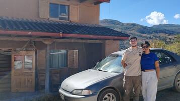 A building with a corrugated metal roof, a wooden door, and a car parked in front.