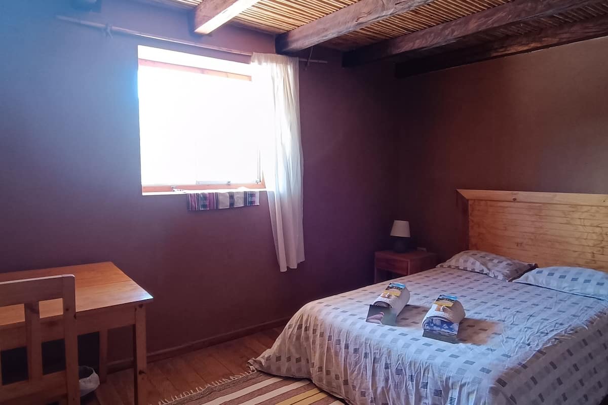 A bedroom with a wooden bed, a small desk, and a window with curtains.