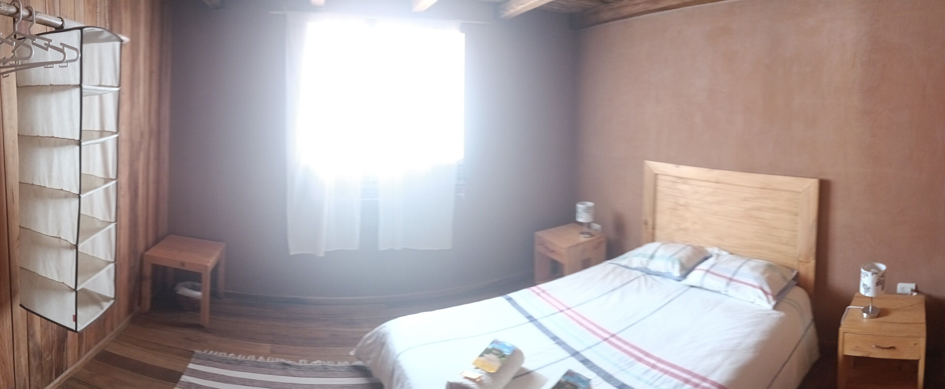 Un dormitorio con cabecera de madera, cama con colcha escocesa, mesita de noche con lámpara y una pequeña mesa de madera.