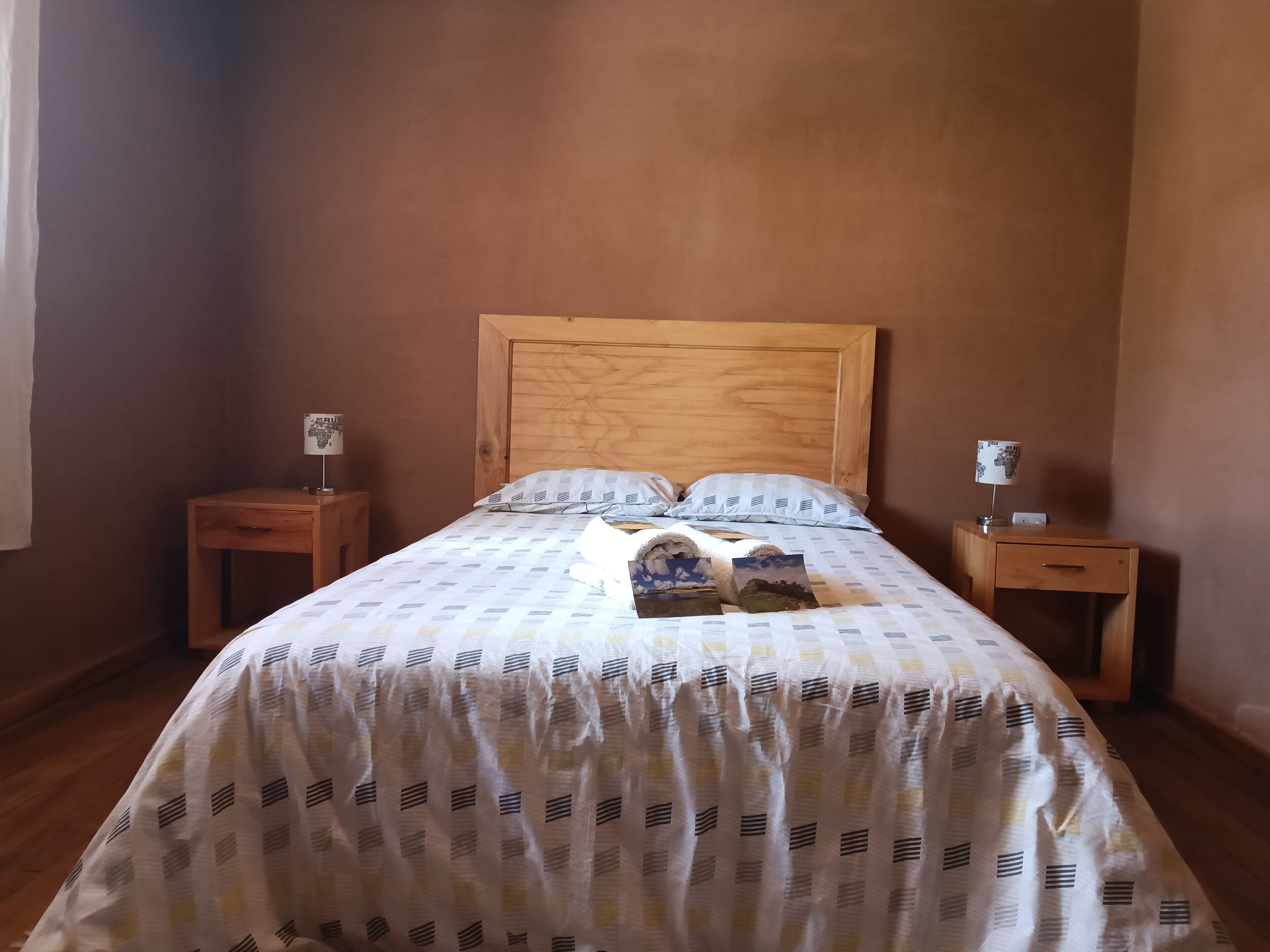 Una cama bien hecha con un edredón estampado, dos mesitas de noche con lámparas y un cabecero de madera.